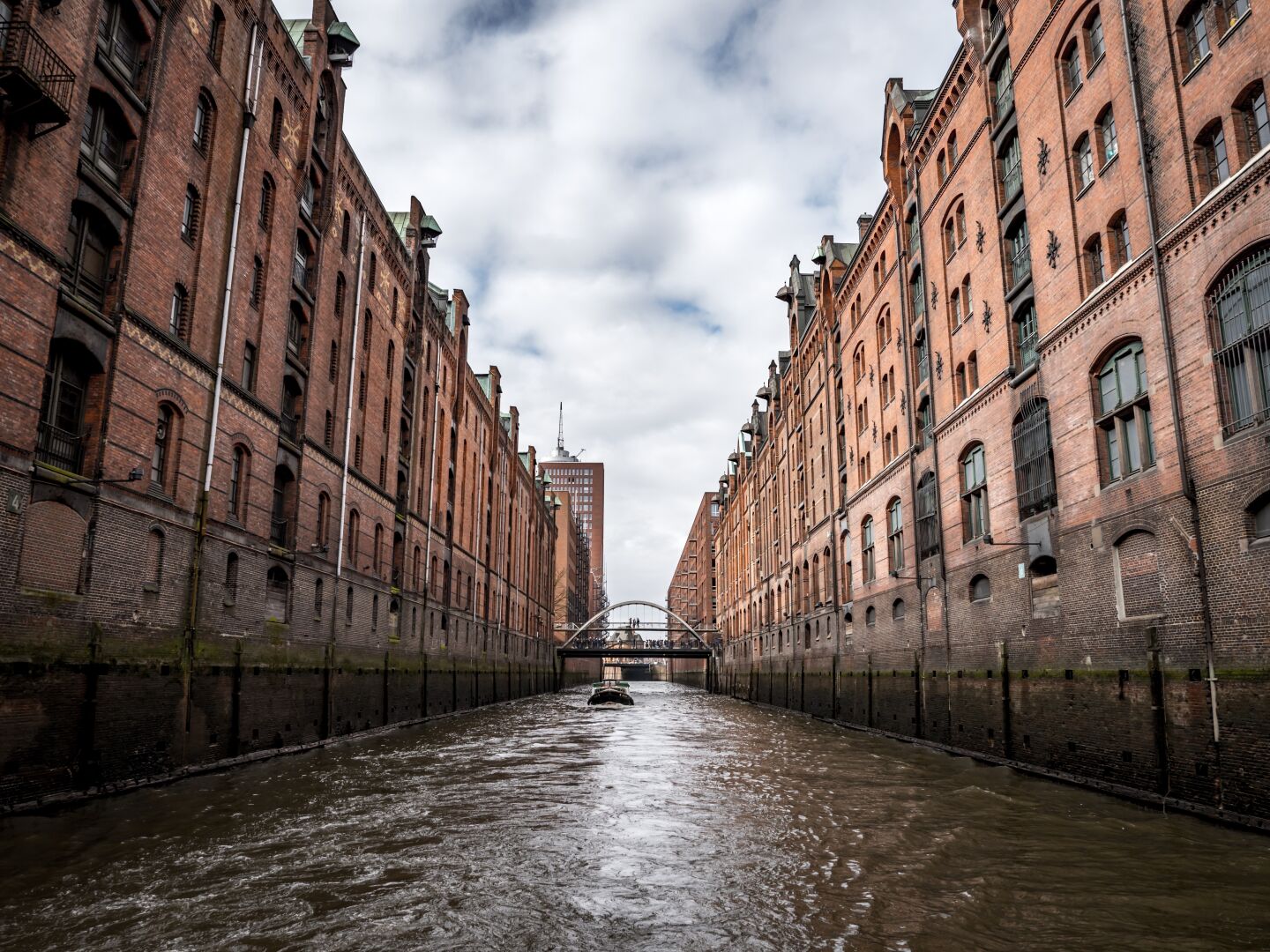 Red brick buildings left and right of a canal, with the image taken from a boat on the canal