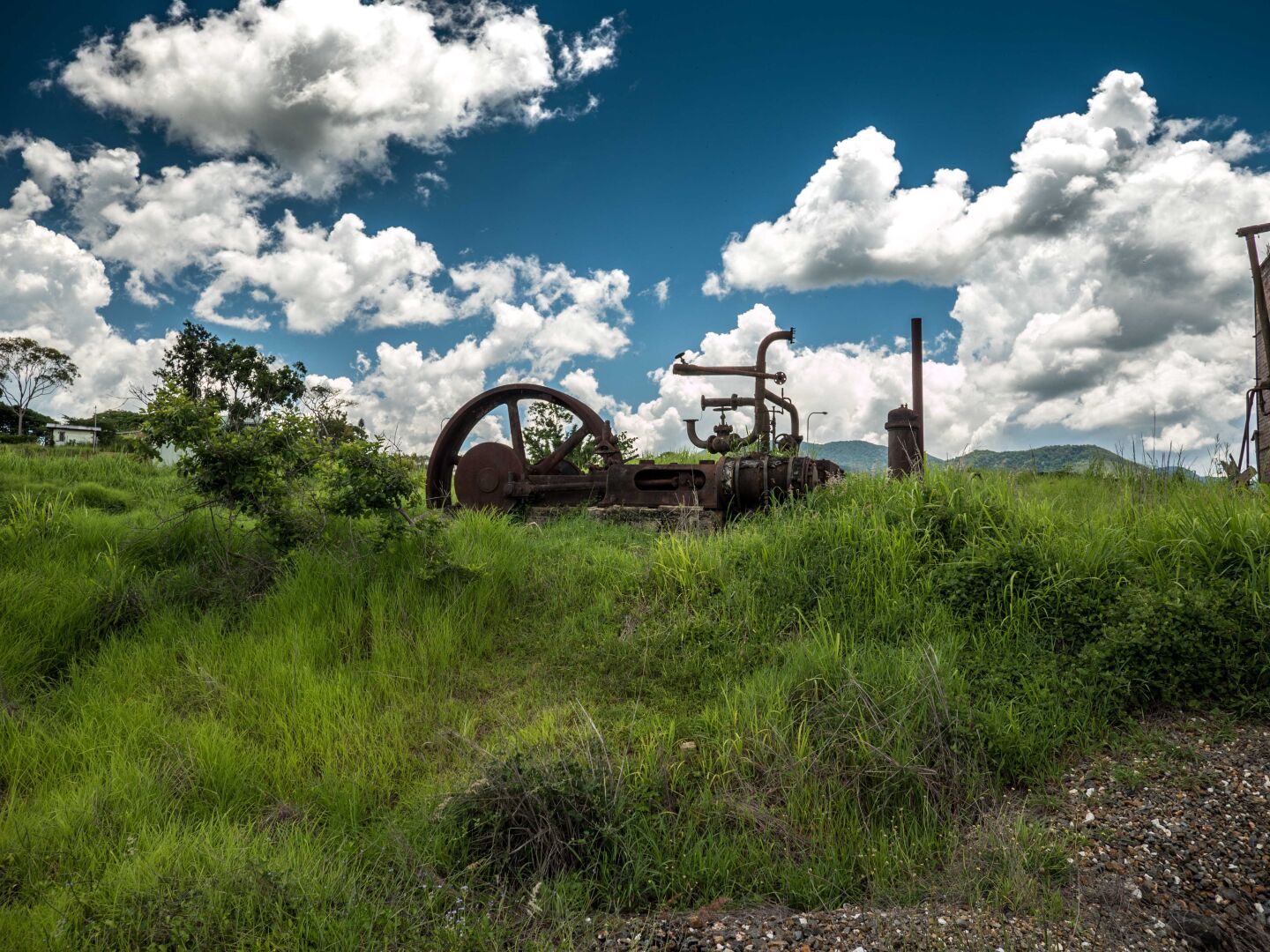 Old mining equipment out of rusted steel and something that looks like a wheel sits in the middle of a green meadow