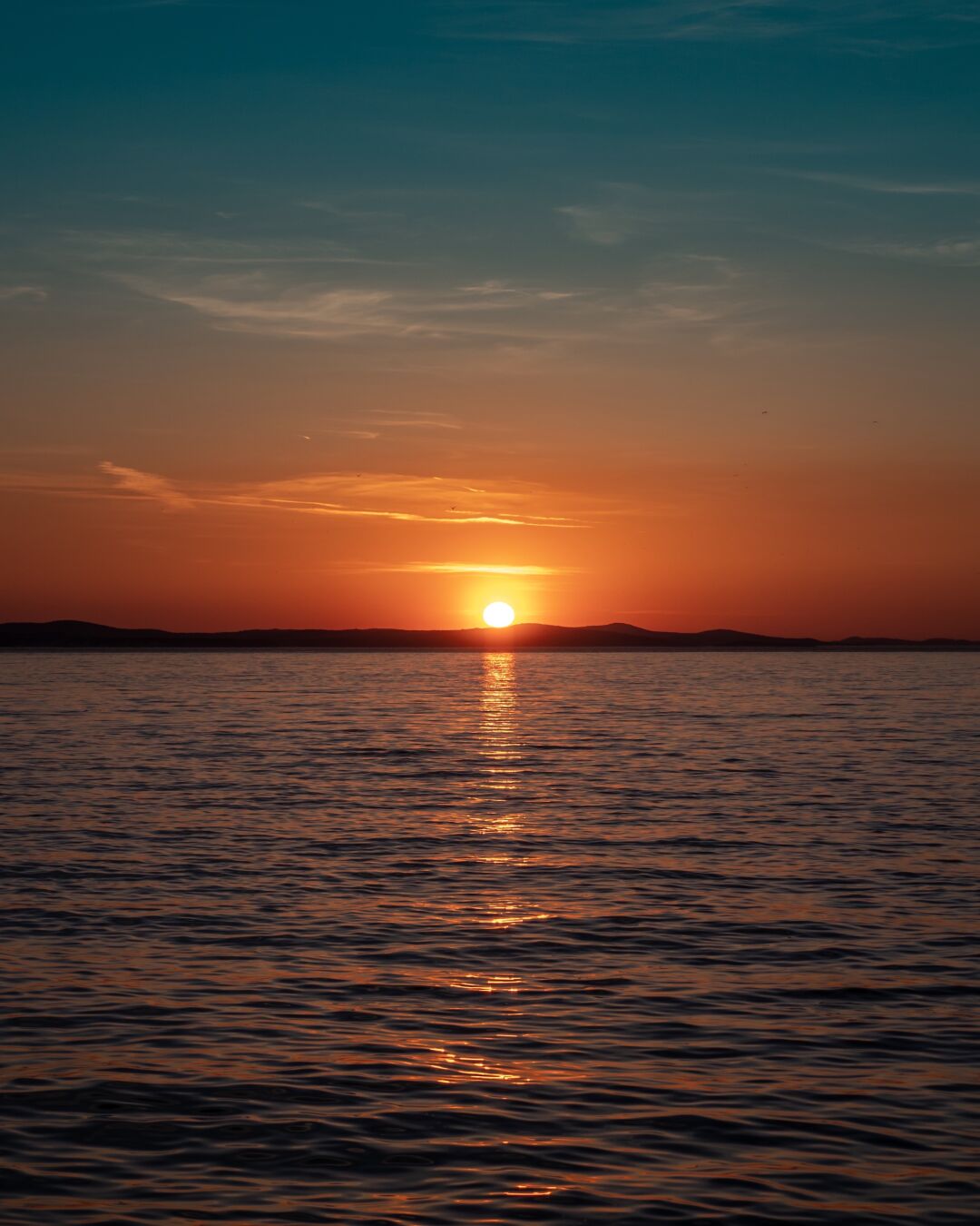The sun is setting in the distance, casting a way of light onto the water in front of the viewer