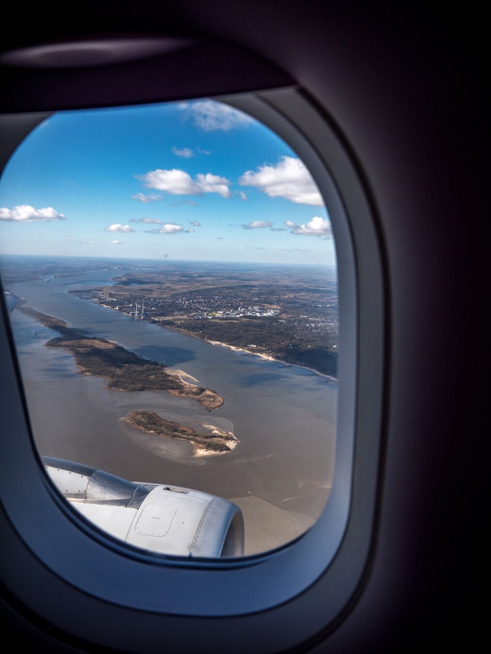 View out of an airplane window along a big river running towards the sea