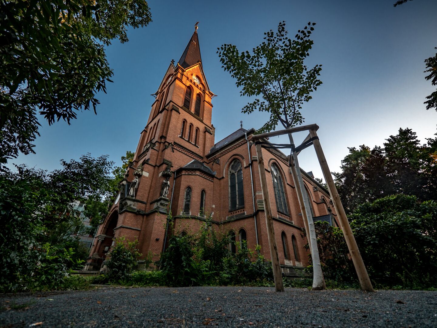 A brick church surrounded by trees with its tower top still in the setting sunlight while the rest is already in the shadow