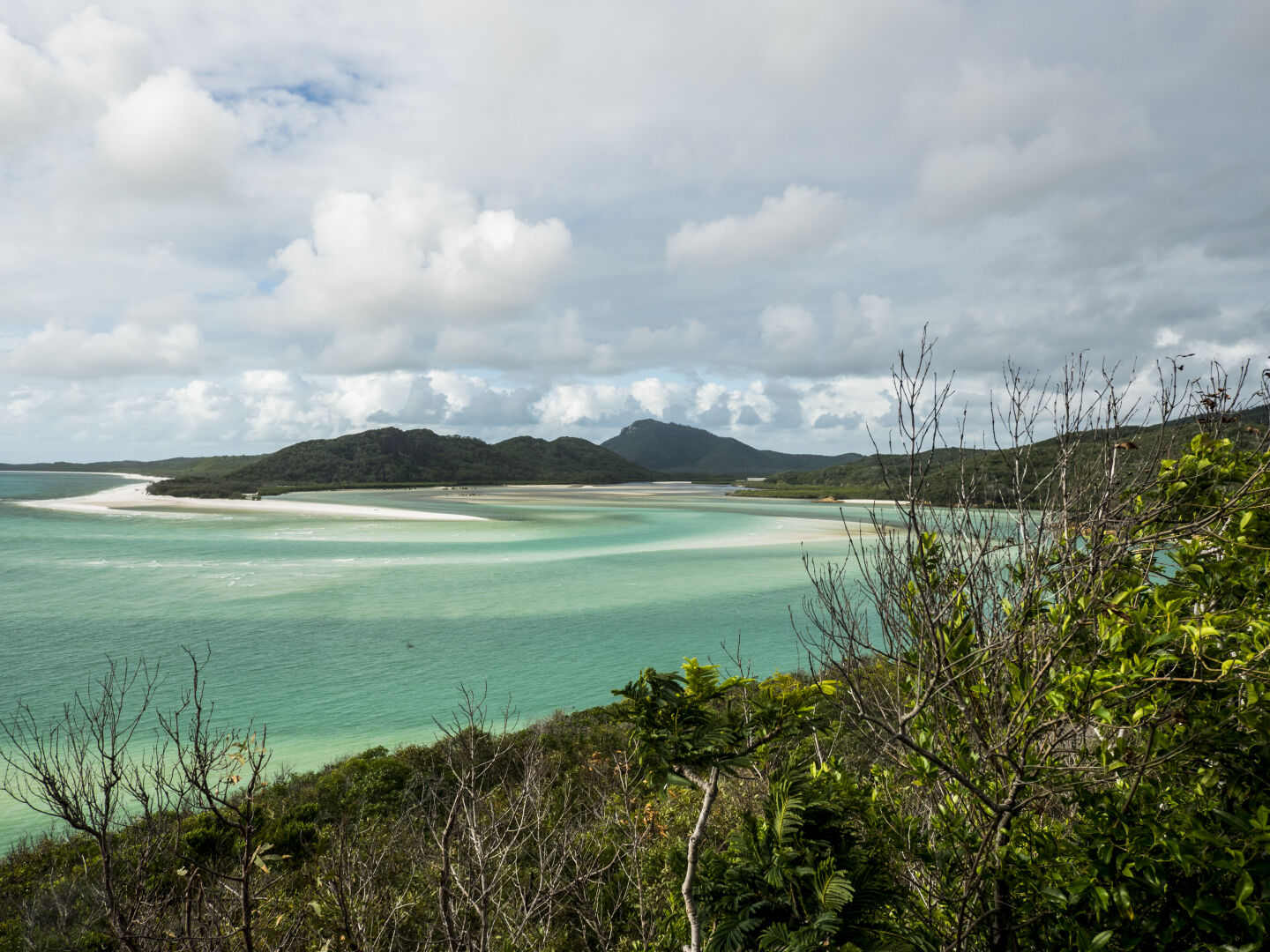 A blue lagoon with extremely white sand and green hills on the right and in the background