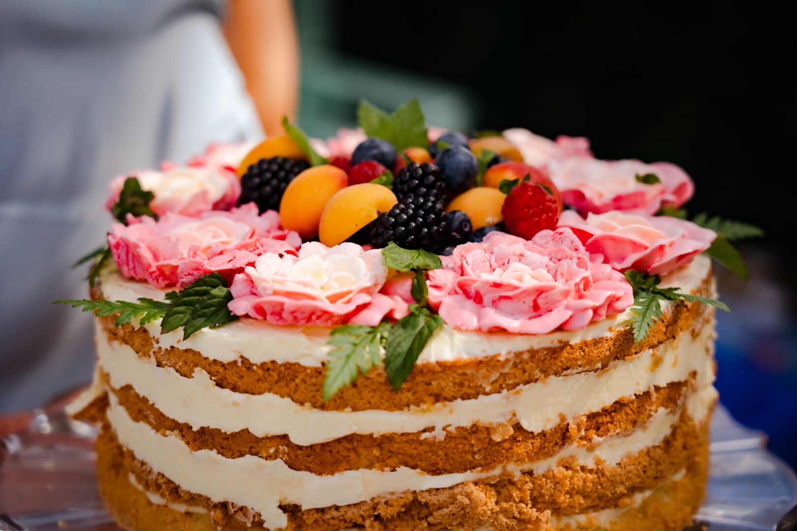 A cake with multiple layers, decorated with flowers and colourful fruits on top