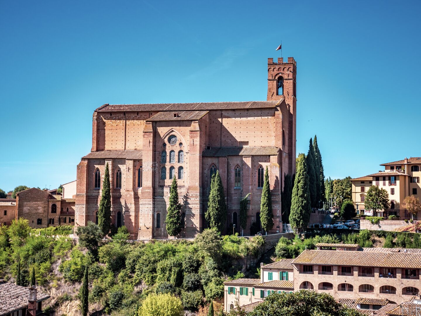A big church sits on a hill, surrounded by small houses and tall trees. The church feels more like a castle