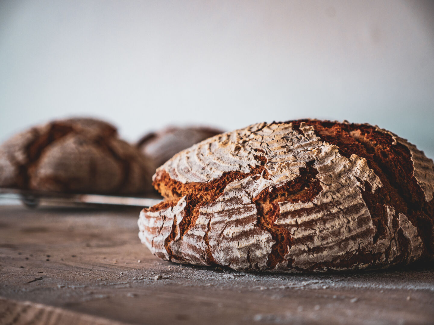 A loaf of bread on a wooden table with a few more loafs behind it