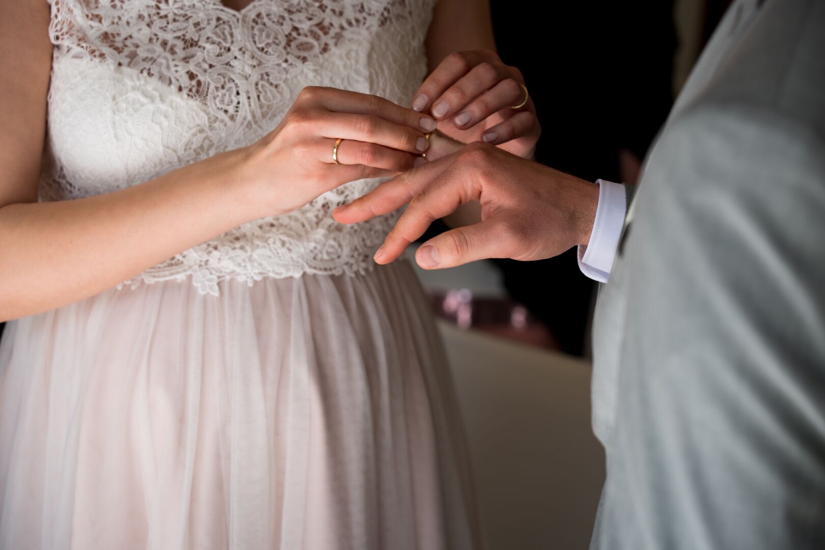 The bride with her wedding ring already on her finger places the ring on the hand of the groom