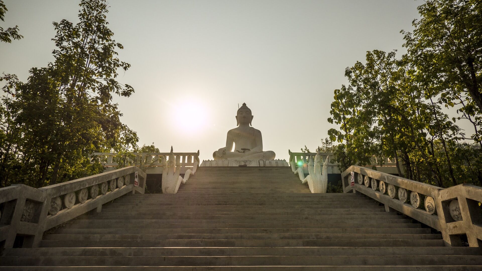 A Buddha statue with stairs leading up to it and the sun setting in the background