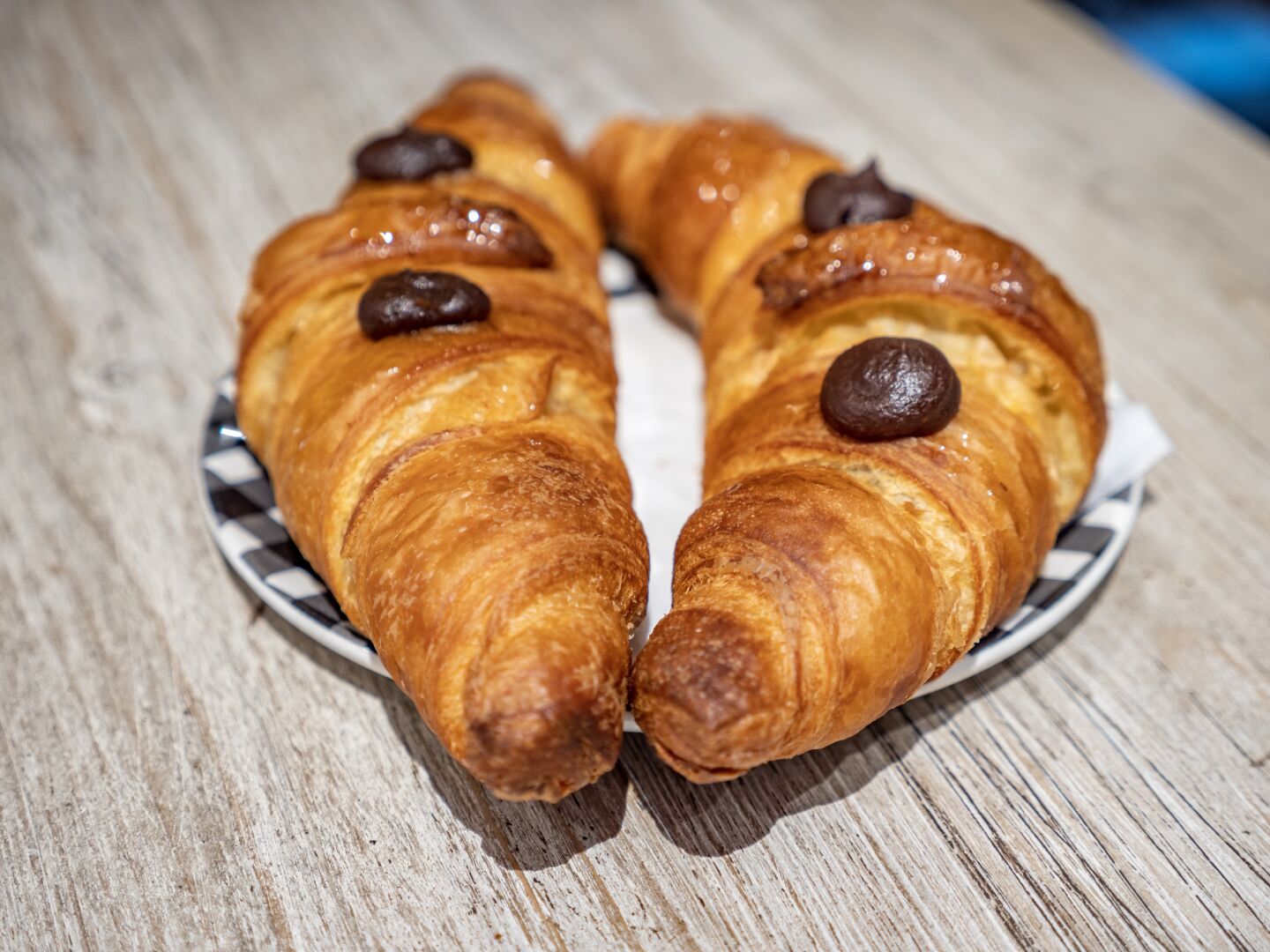 Two croissants side by side on a small plate with chocolate parts on top
