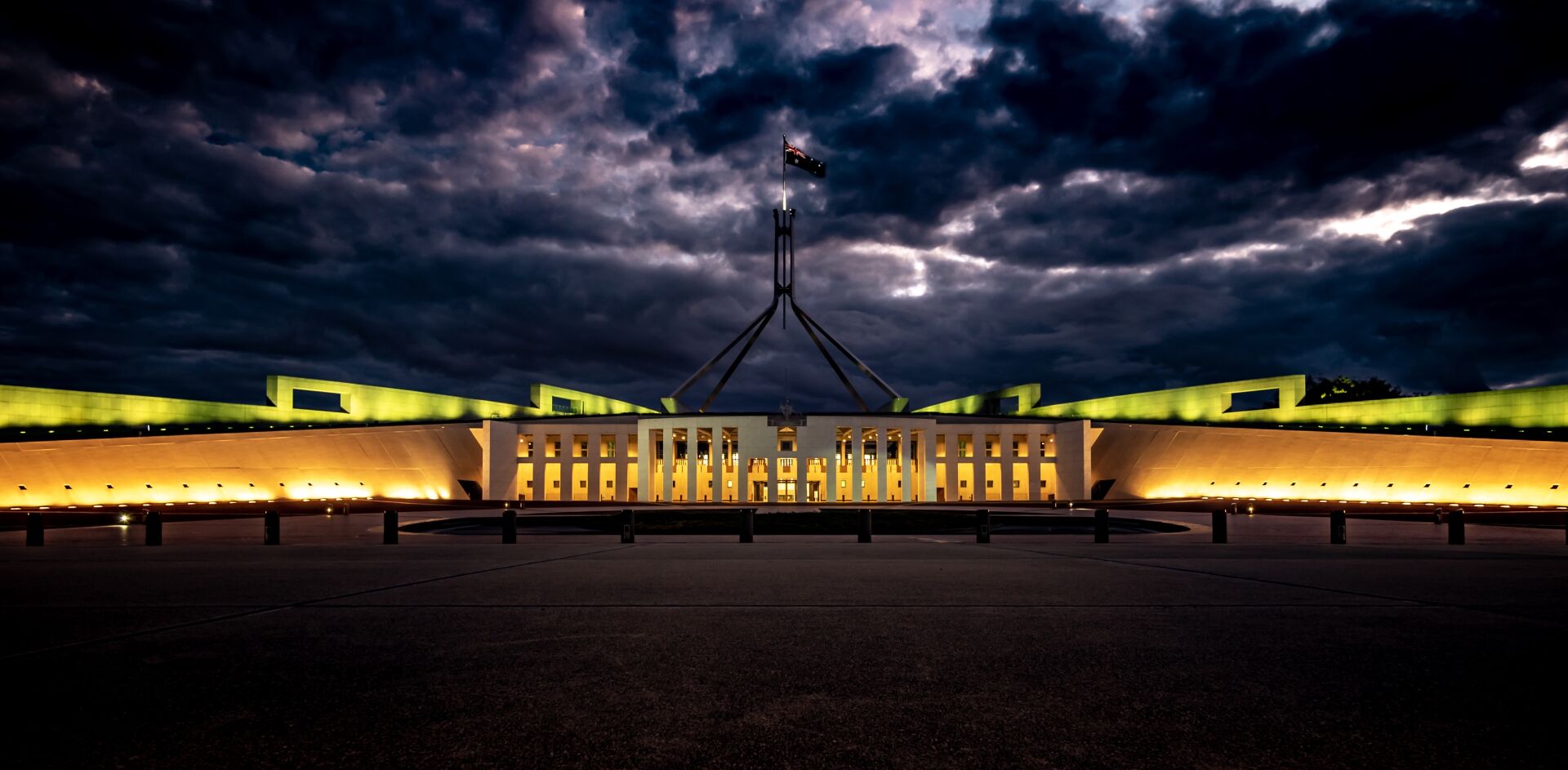 A flat building at night with clouds above and the walls light up in orange