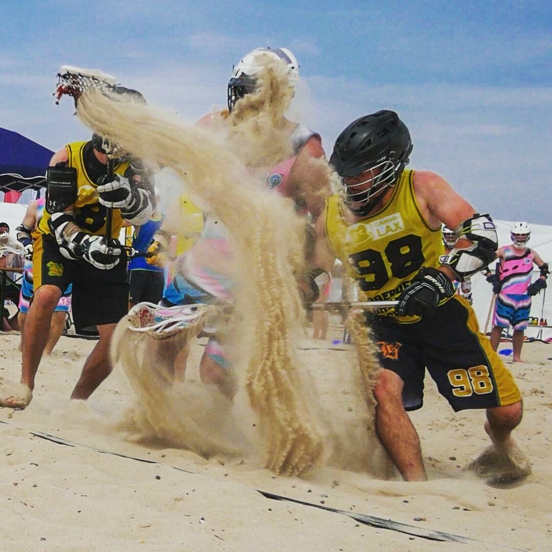 The players with bats are fighting for a ball on the beach, pulling sand behind them