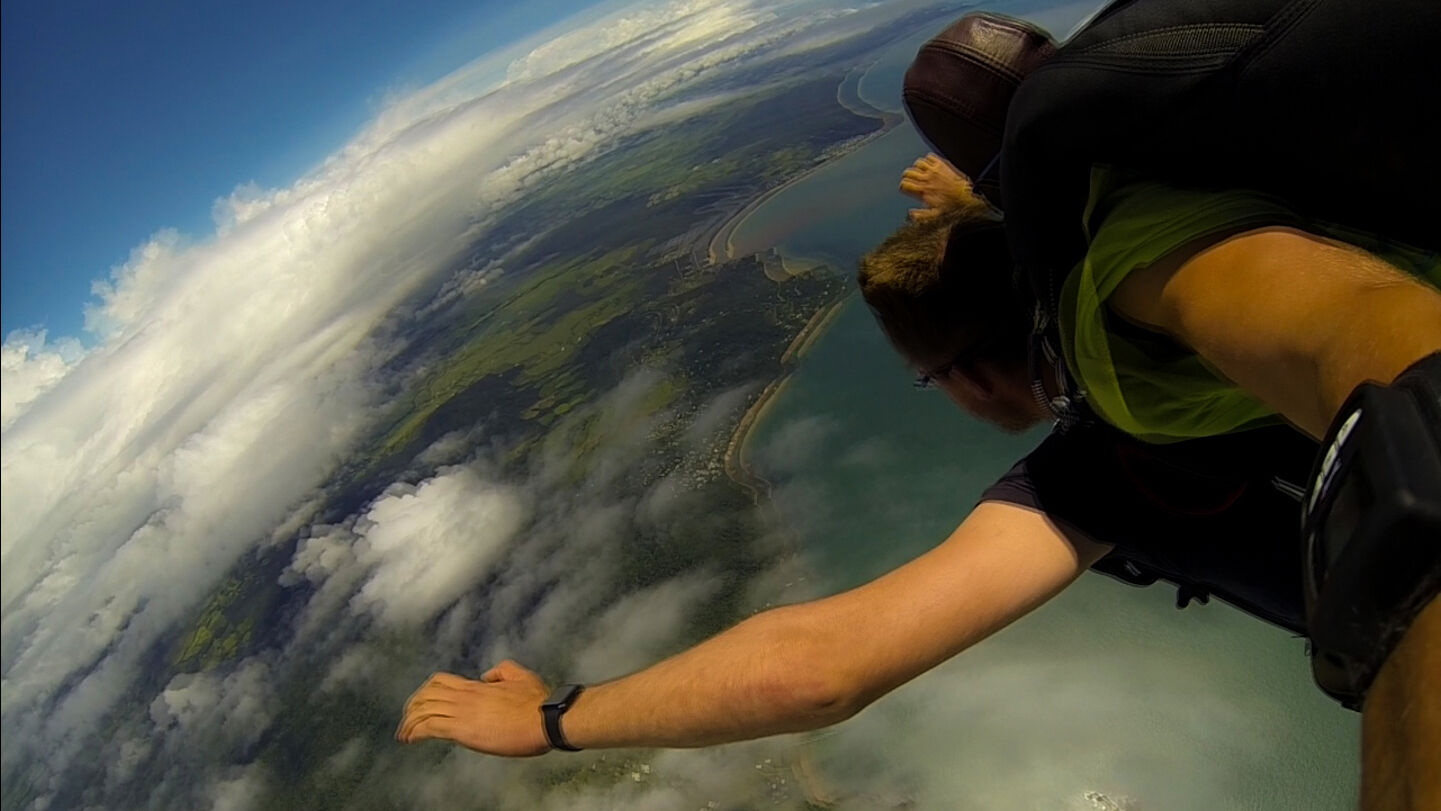 A tandem skydive with the person on top holding the camera, with the earth unsharp below due to the high speed