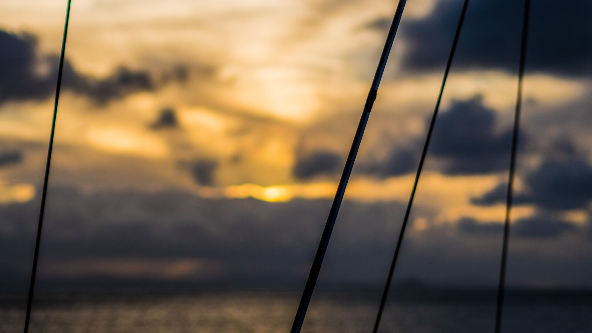 The sun is setting in the distance, with ropes from the boat crossing the view in the foreground