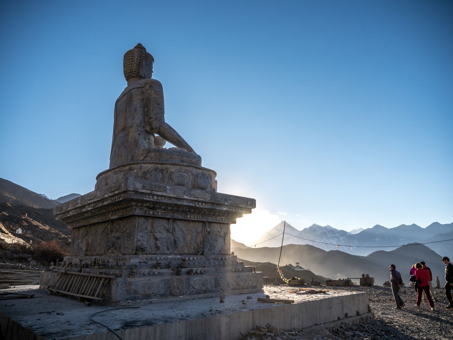A Buddha statue watching the valley, with the setting sun and snow covered mountains in the background