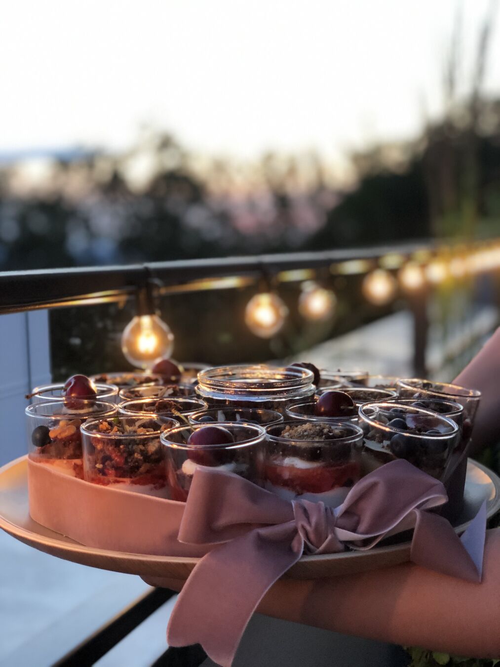 A plate with multiple small containers made out of glass filled with cream and topped with crunch. In the background the lights of the balcony