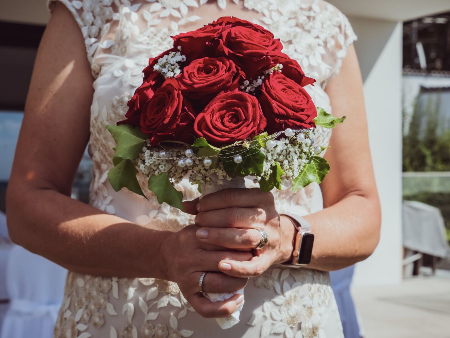 A bride in a white dress holds red roses