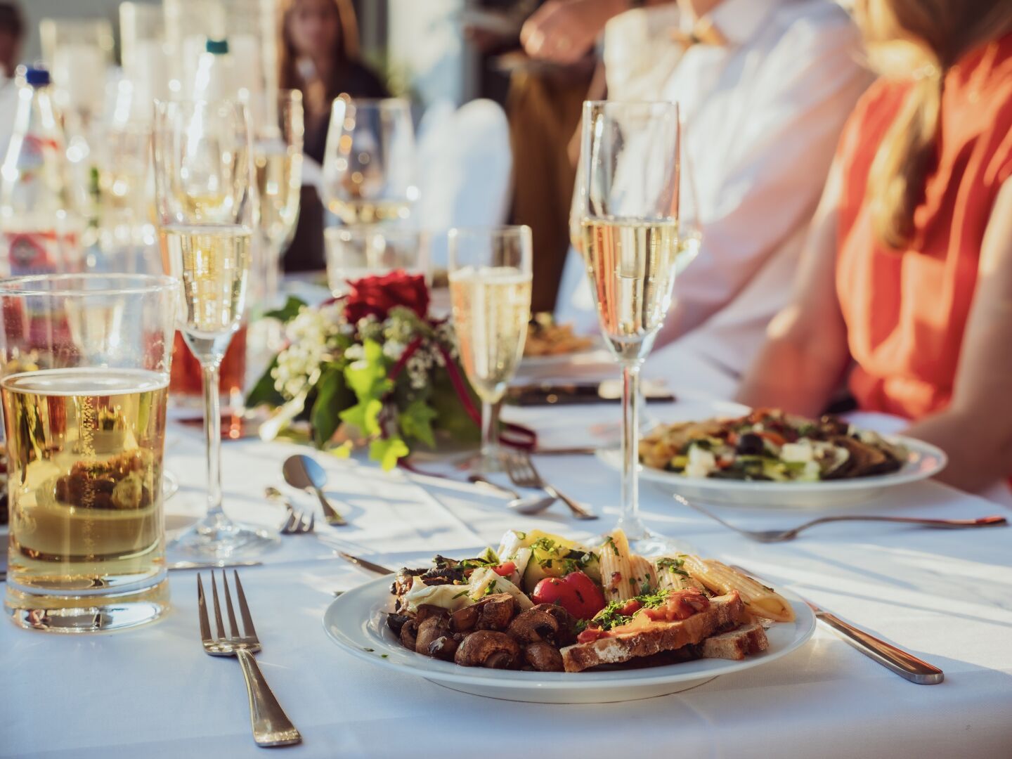 Plates full of food, glasses with champagne and people dressed in pretty clothes and dresses. Focus is on the filled plate