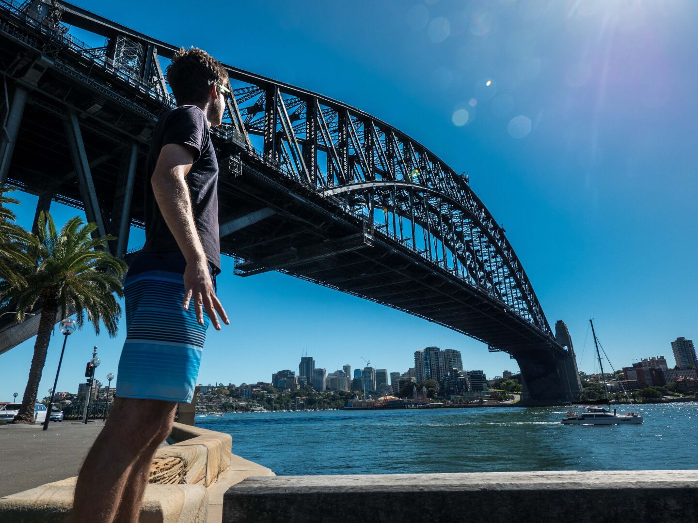 A man with short trousers standing on a pier, with the harbour bridge behind and above him