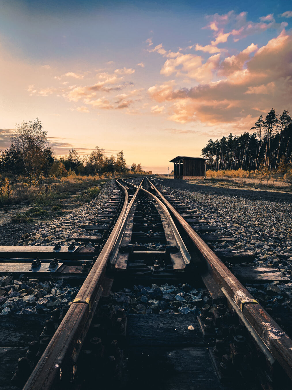 Tracks and a switch of a narrow gauge railway lead into the distance. The light is red as sunset is near.