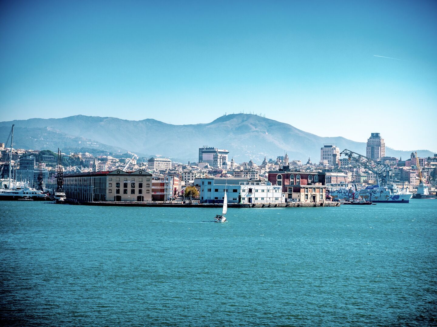 Picture taken from a boat with the sea on front and a city with a big harbour in the background. Behind that a few hills are visible
