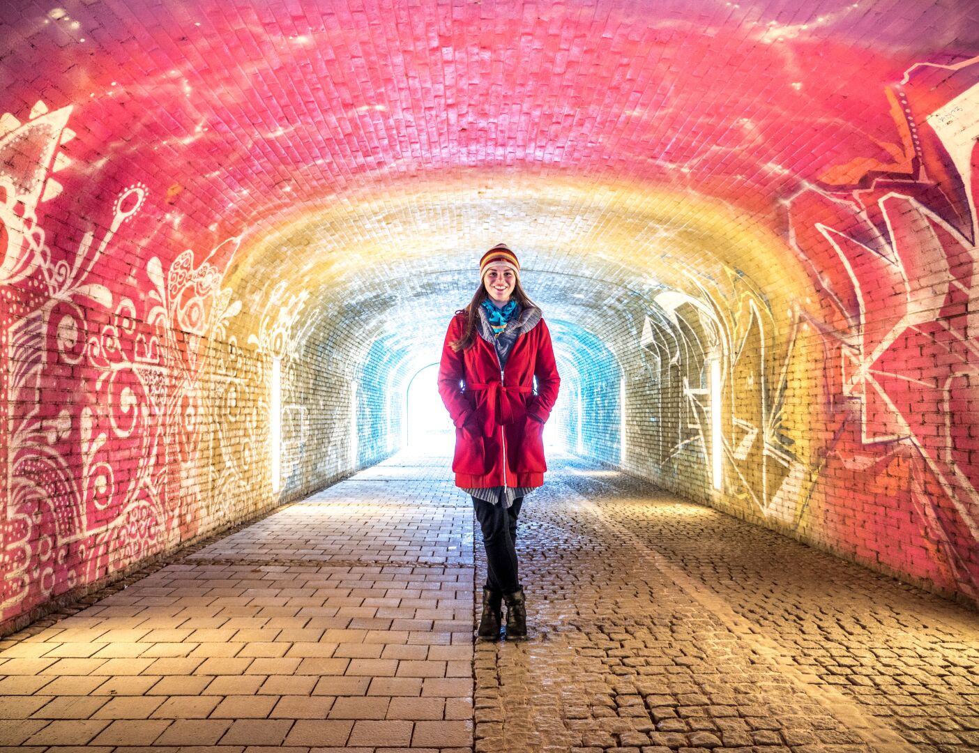 A woman in a red coat standing in a tunnel with walls that are painted in different colours